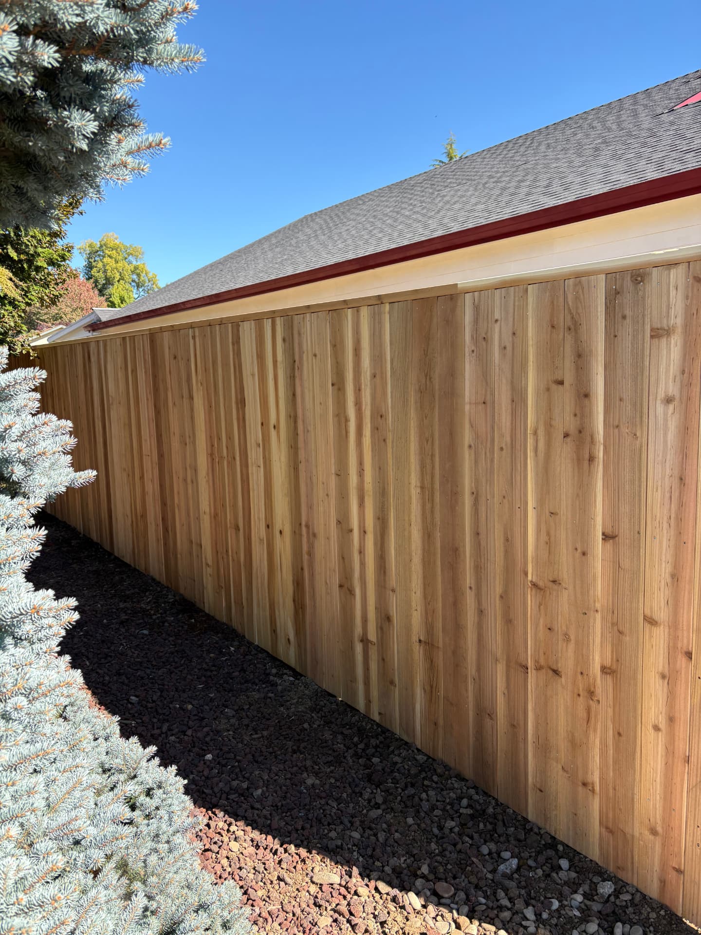 Japanese cedar picket fence running along the side of a house next to a gravel path